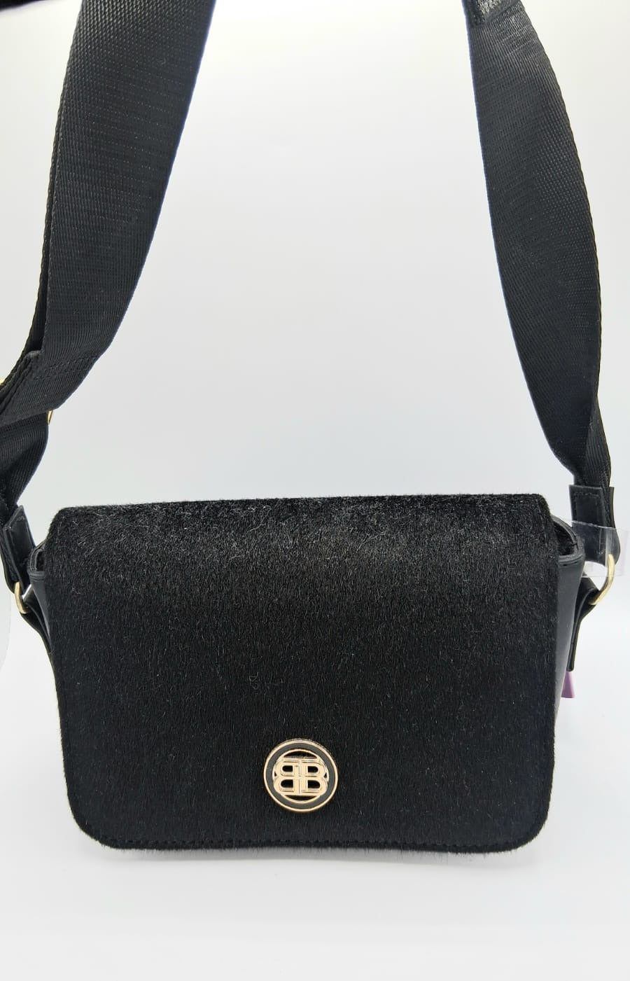Crossbody bag negra con correa ancha ajustable y detalle metálico dorado en el frente.