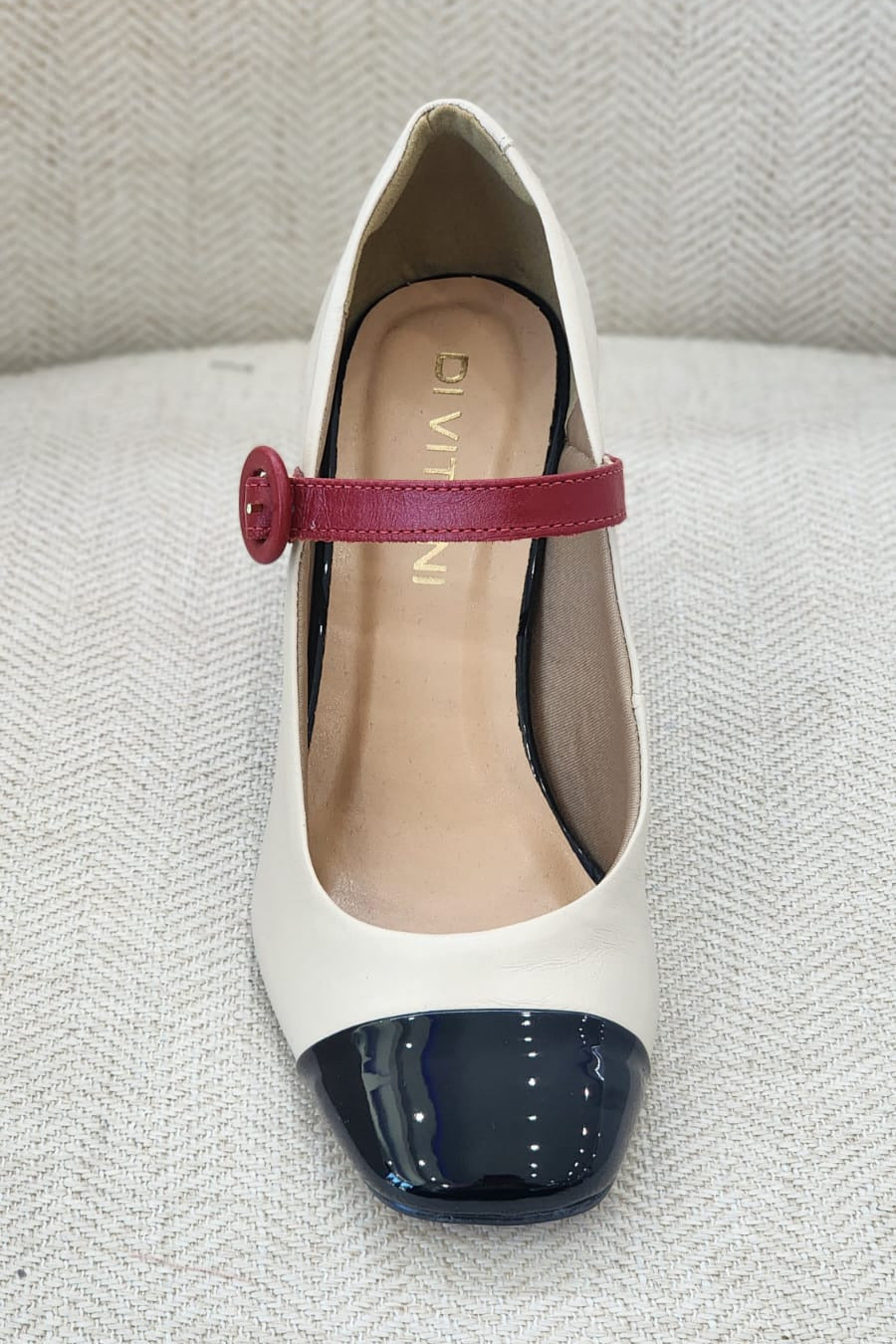 Vista frontal de zapato con punta negra brillante, correa roja y acabado sofisticado.