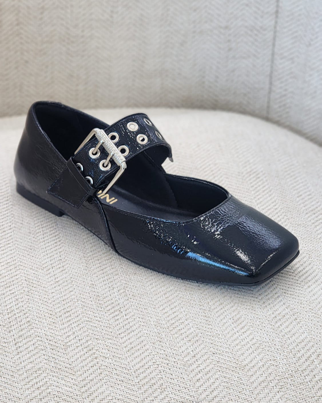 Vista lateral de zapato plano negro elegante con punta cuadrada.