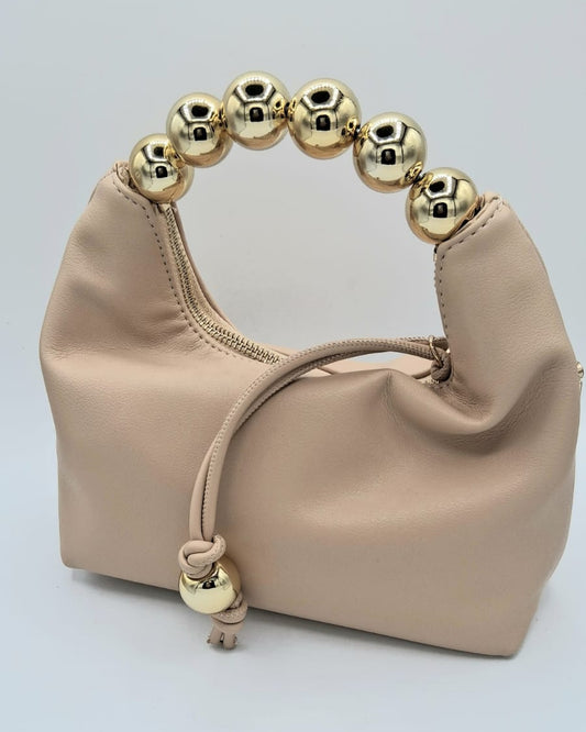 Cartera nude con mango de esferas metálicas doradas y detalle de borla decorativa.