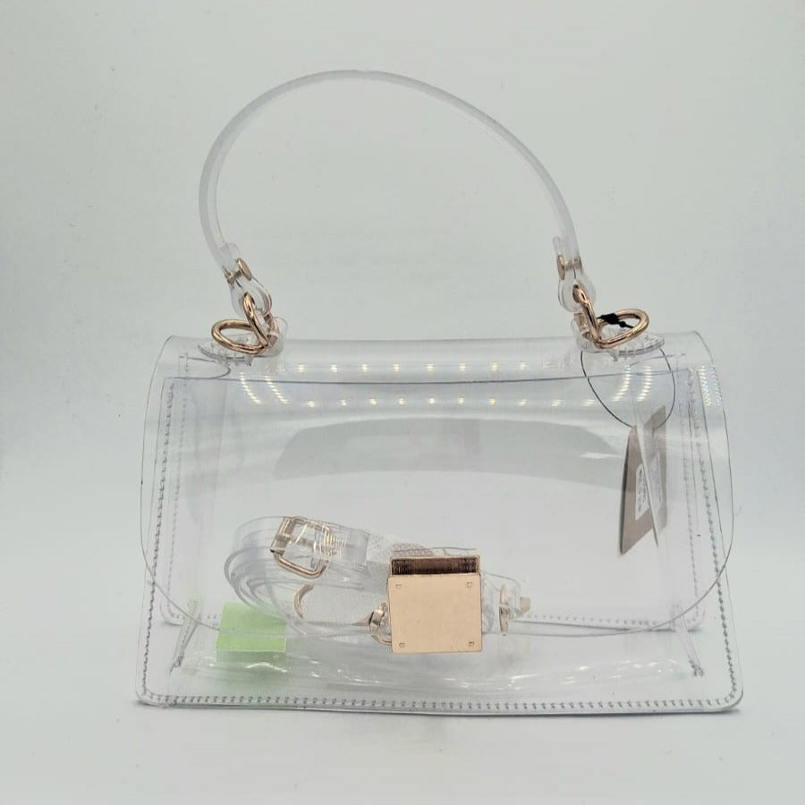 Cartera transparente rígida con cierre dorado y correa larga removible.