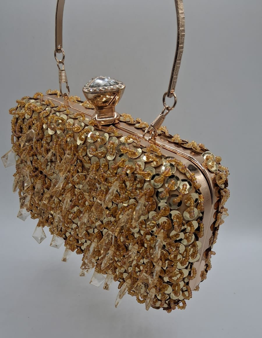 Clutch rígido dorado con lentejuelas y pedrería colgante, cierre con broche joya.