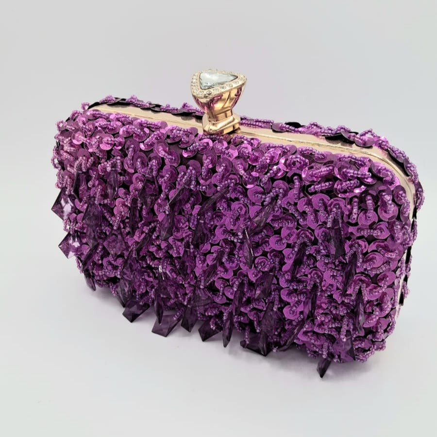 Clutch rígido morado con lentejuelas y pedrería colgante, detalle de cierre tipo joya.