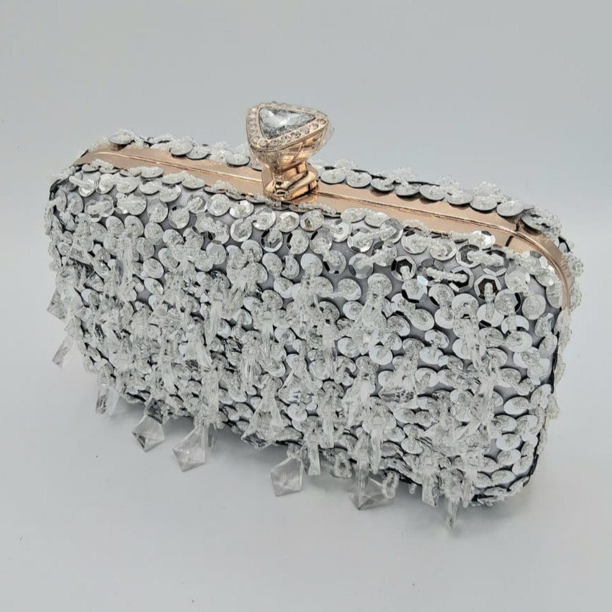 Clutch rígido plateado con lentejuelas y pedrería colgante, broche joya superior.