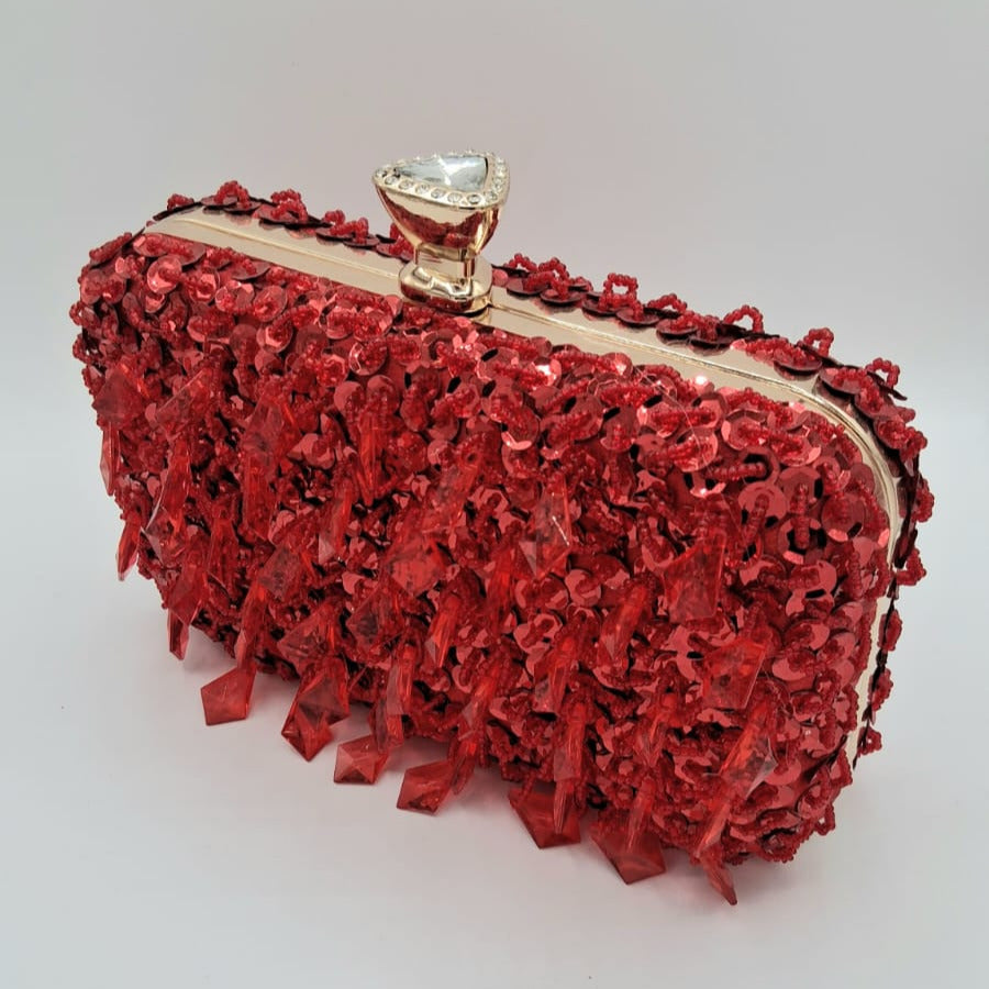 Clutch rígido rojo brillante con lentejuelas y pedrería colgante, detalle de broche en forma de diamante.
