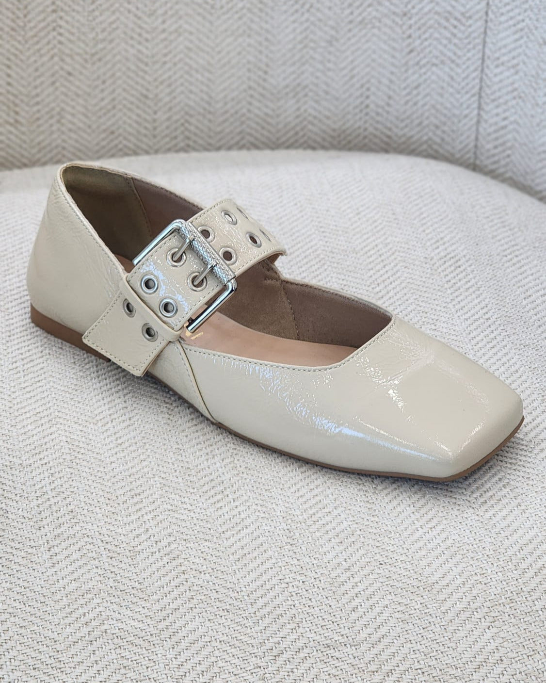 Zapato plano en charol off white con hebilla metálica ancha.