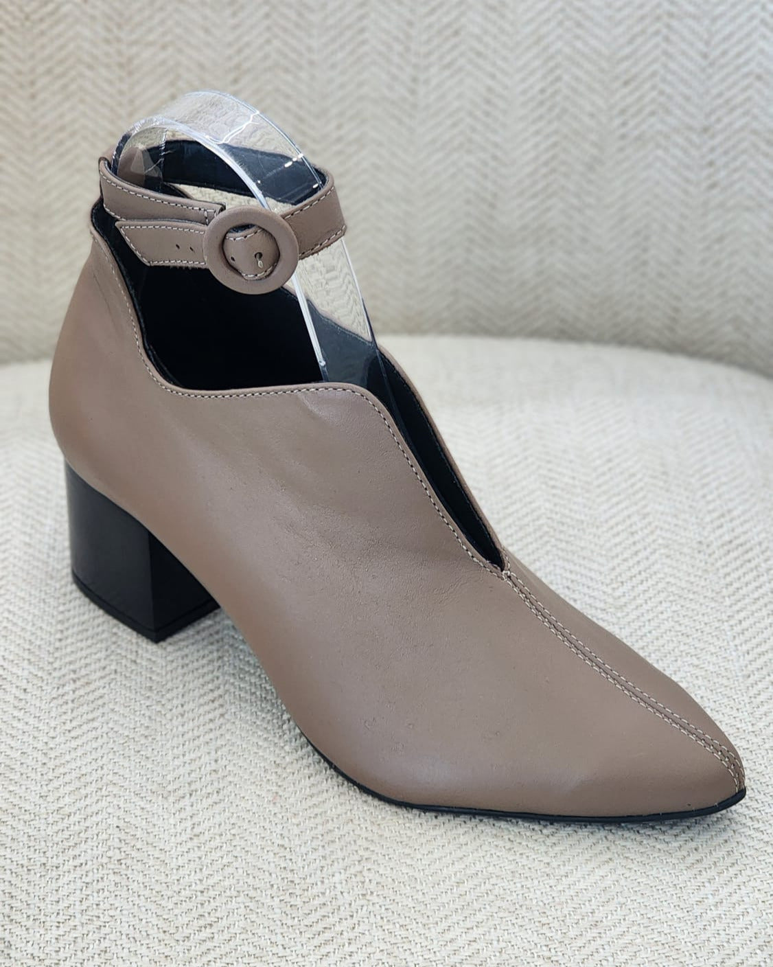 Zapato beige de tacón bloque medio con punta afilada y correa al tobillo sobre fondo crema.