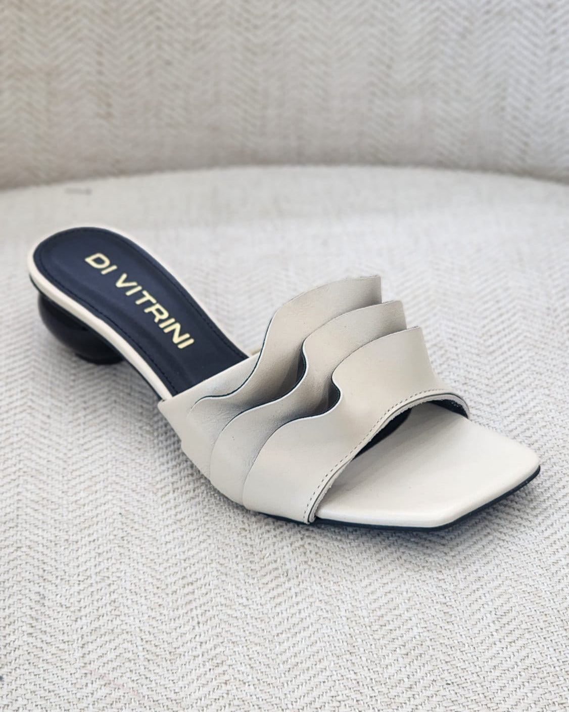 Sandalia off white con tiras onduladas en el empeine, punta cuadrada y tacón bajo.