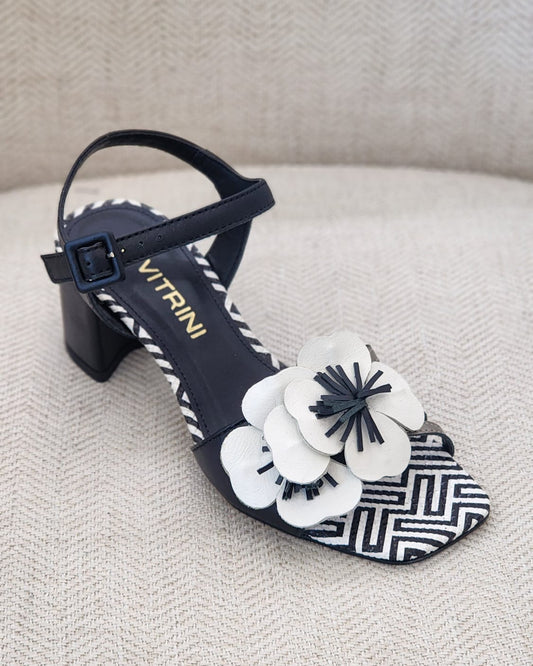 Sandalia preta con flor blanca en relieve, tacón bloque bajo y suela estampada en blanco y negro.