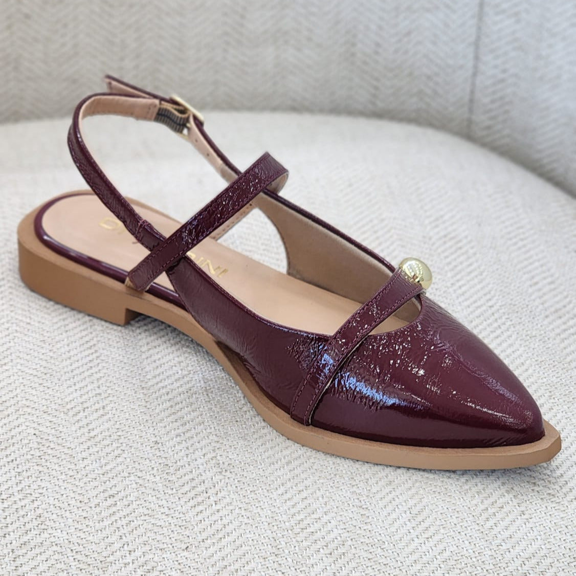Vista lateral de zapato plano burgundy elegante con pulsera y suela baja.