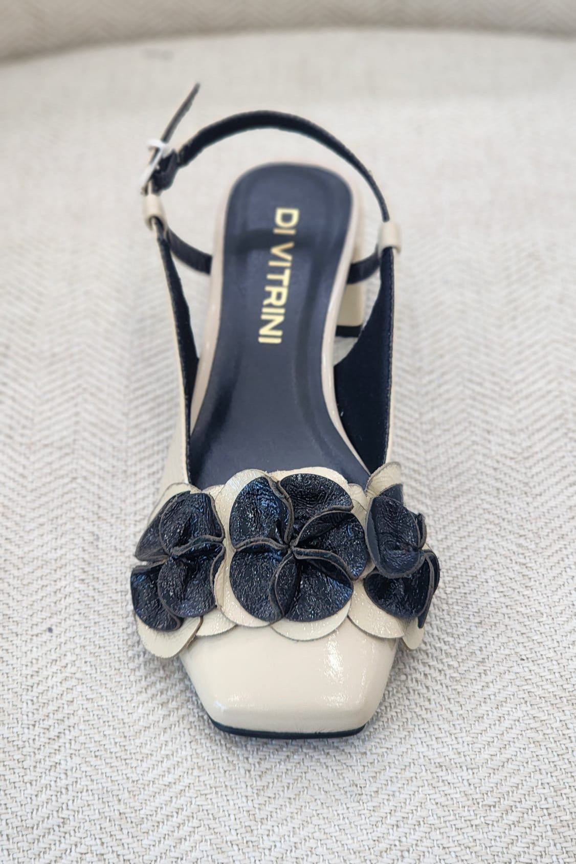 Sandalia bicolor off white y negro con flores decorativas en relieve, punta cuadrada y tacón bajo.