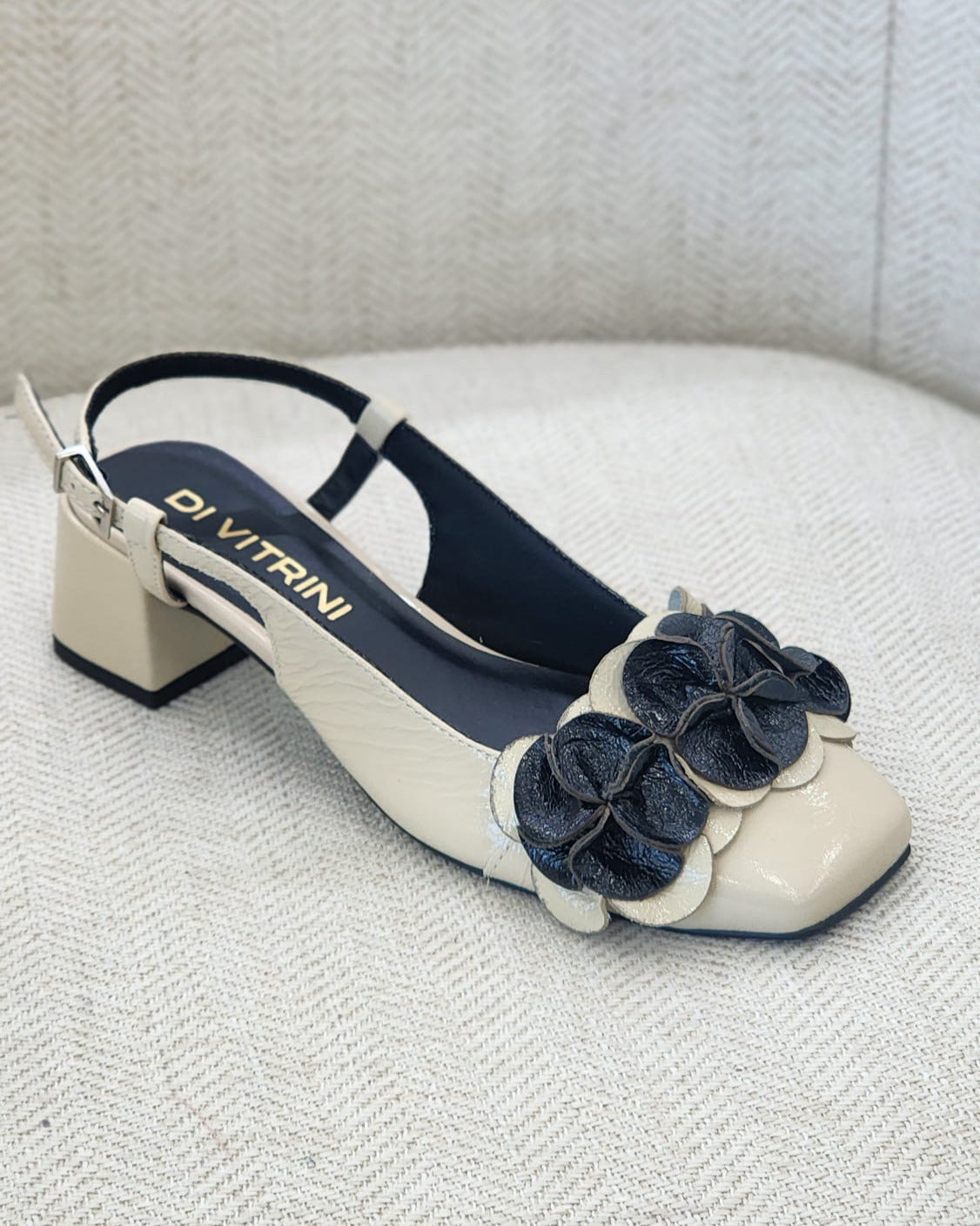 Vista lateral de sandalia off white y negro con diseño floral y correa ajustable al tobillo.