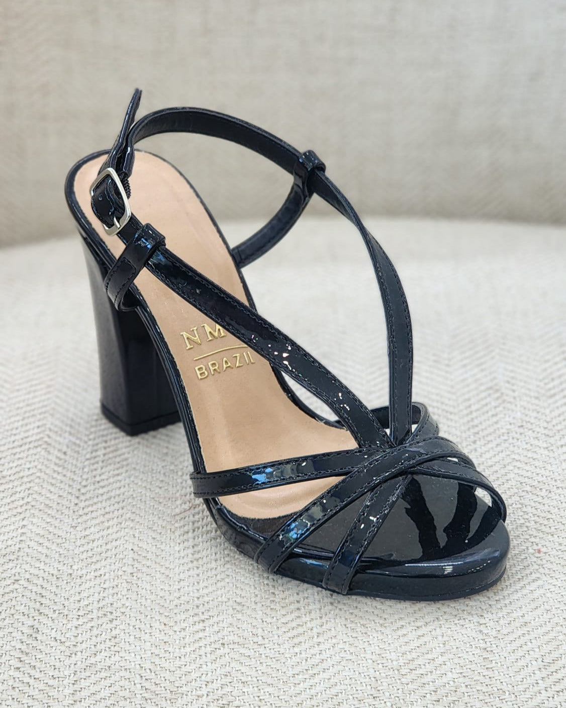 Vista lateral de sandalia negra brillante con tiras finas y correa ajustable al tobillo.